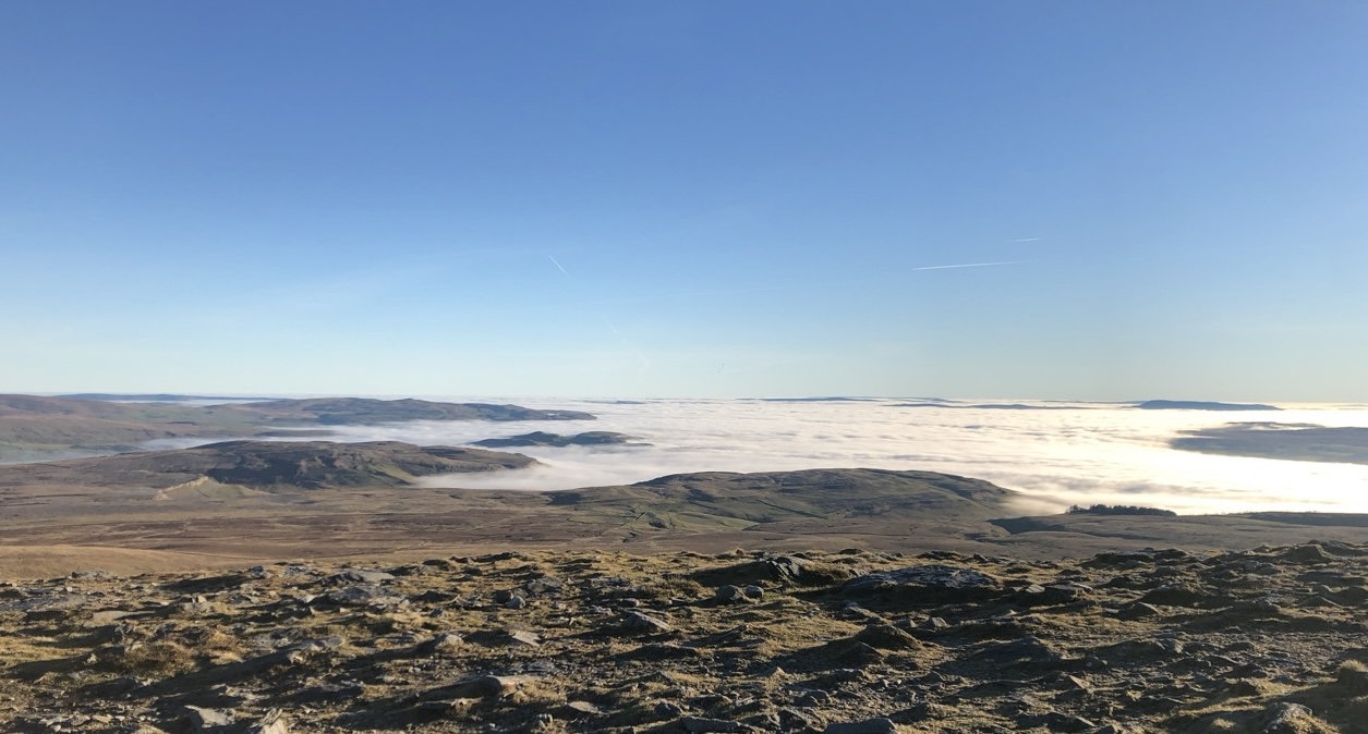 A panoramic view of mountains on a clear day. The valley below is coverd by fog.